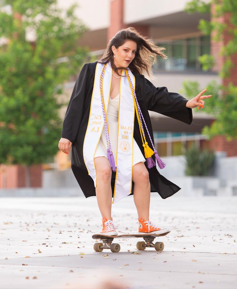 A graduate posing for a photo on a skateboard.