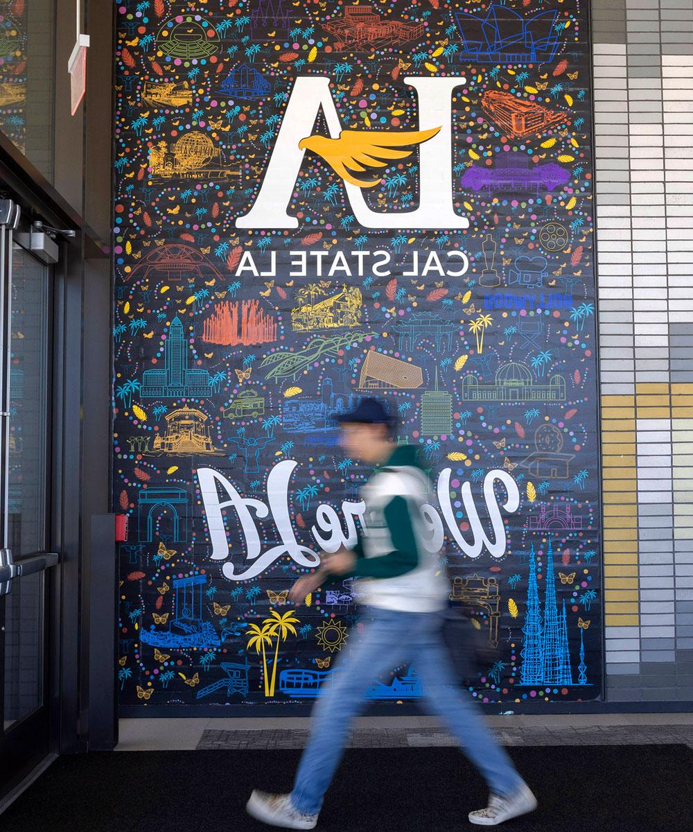 A person walking in front of a mural.